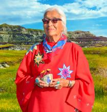 A woamn in traditional dress stands with a mountain in the background.