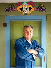 A man poses infront of a doorway crowned with a painted sculpture.