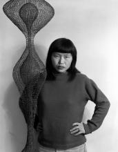 Woman with medium black hair wearing a sweatshirt in front of hanging wire artwork. 