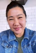 Irene Pak Lee, who is a Korean American woman. She wears a denim jacket and smiles quietly at the camera