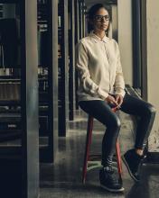 Woman wearing glasses and a beige sweater sitting on a chair. 