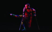 Man with short hair and beard on crutches dancing on stage. 