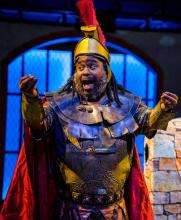 African American man on stage in full medieval battle gear with a red plume on his helmet