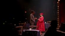 a man and woman stand on a set resembling a jazz bar