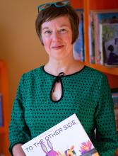 A woman posese for the camera with a book in her hands.