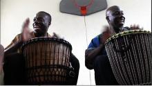 Two men playing drums in a gym. 