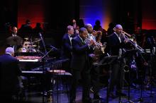 Five Black men and one white man, wearing black suits, perform on stage