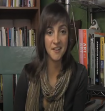 Woman talking in front of bookshelves.