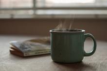 A steaming green mug next to a small paperback book.