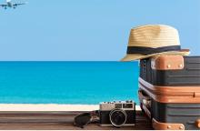 A plane flies over a beach. A cream hat is sitting on two suitcases