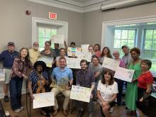 A group of people posing for photo, holding up artwork they have done. 