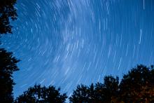 arcs of light in a darkening sky with a line of trees at bottom of frame