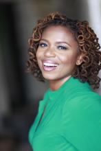 a smiling African-American woman with curly locs wearing a green blouse