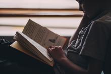 a young child sitting in a window reading a book