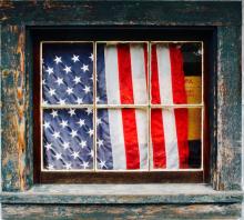 an American flag hangs curtain-like inside a blue wood-framed window