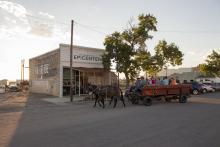 people in horse drawn cart in front of low building