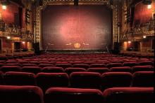 a theater auditorium with red velvet seats, boxes, a proscenium arch and a painted fire curtain