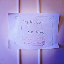 Close-up of a door with stickie note that says "Shhh, I am reading. Please knock. Thank you mum"