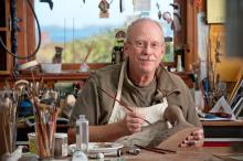 a man sitting in a workshop carving a duck decoy