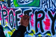 a hand holding a paintbrush working on a wall mural that says poetry