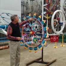 A man shows off a whirligig which is like a looks like a decorated spinning wheel