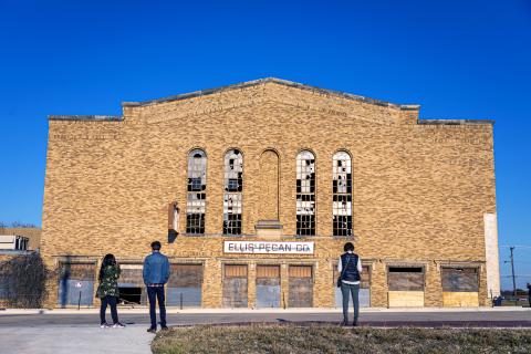 A large brick building with large windows that have been broken.