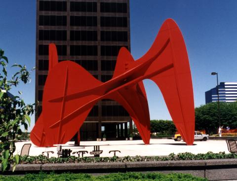 A huge red iron sculpture next to a black building. 