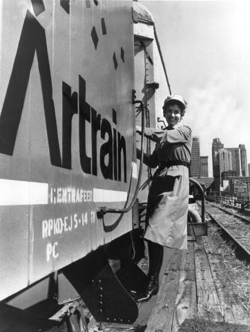 Woman in dress holding on to the side of a train. 