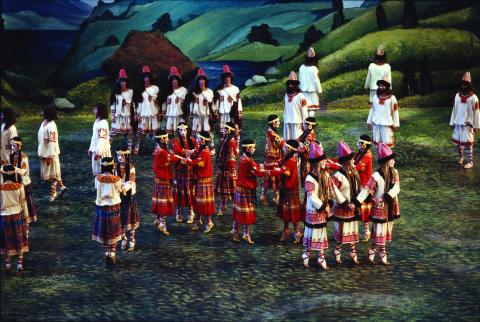 Dancers dressed in elaborate red and white costumes, wearing long black wigs and their faces painted, on stage. 