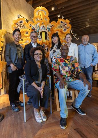Group of people posing for a photograph in front of a Black Masking suit with yellow feathers and beading