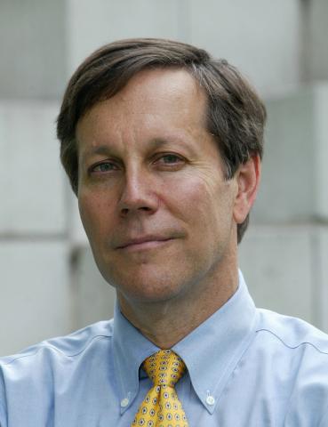 Portrait of white man with brown hair wearing a blue shirt and yellow tie.