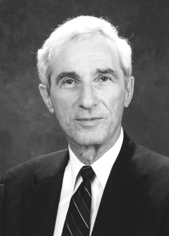 Portrait of white man with white hair wearing a dark suit. 