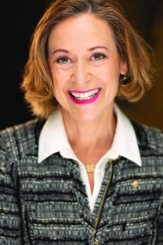 Portrait of a woman with short brown hair, smiling, wearing a blue striped sweater over a white shirt.