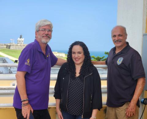 A man with gray hair and goatee, wearing glasses and a blue shirt; woman with long dark hair wearing a black shirt; bald man with moustache where dark blue shirt. 