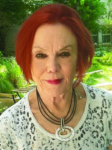 Portrait of an older woman with red hair wearing a lacy top outdoors.