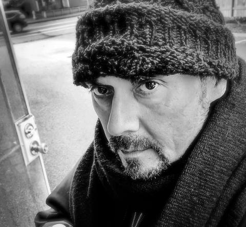 Black and white photo of man with a goatee wearing wool hat and a heavy coat standing in doorway.