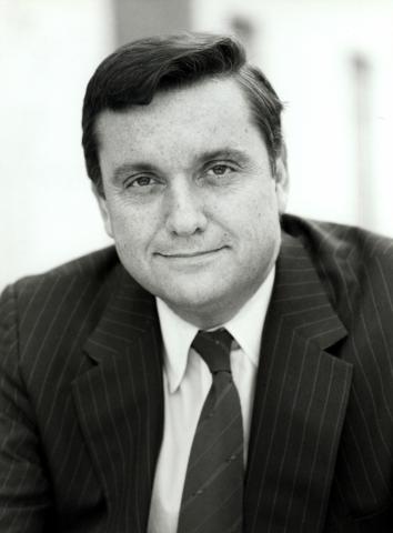 Portrait of white man with short dark hair in dark suit, white shirt, dark tie
