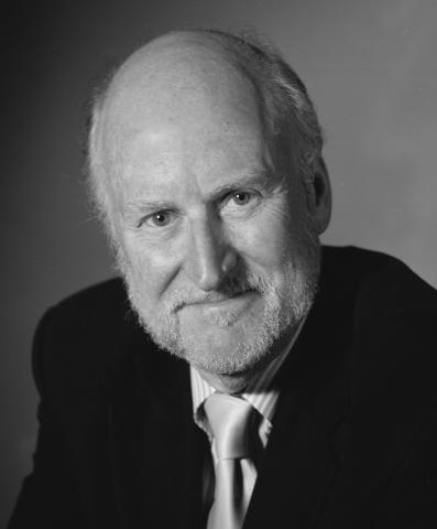 Portrait of white bald man with a beard wearing a dark suit. 