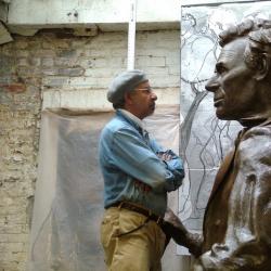 an older African American man stands face to face with a very large size bronze sculpture of Abraham Lincoln