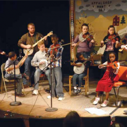a racially diverse group of young people playing fiddles and banjos on a low stage