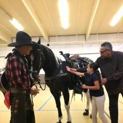 a man in Western wear holds the reins of a horse while a young girl pats the side of the horse