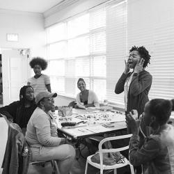 High school students sit around a table while one student stands and speaks