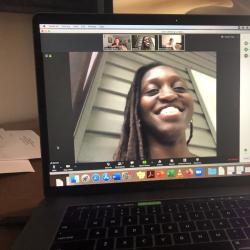 A laptop screen shows a video of a smiling woman with smaller pictures of the people she is speaking with above