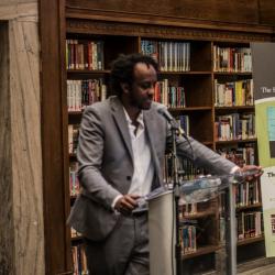 Author standing behind a podium speaking to a crowd of people.