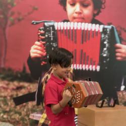 Two young boys play an accordion in front of a large picture of someone playing an accordion