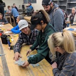 a group of students sitting at a long table making postcards