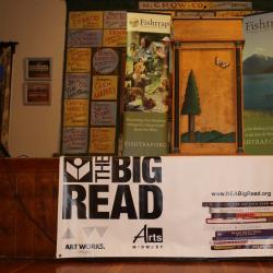 Many colorful posters, a podium, a piano, and a big NEA Big Read banner decorated on a stage.