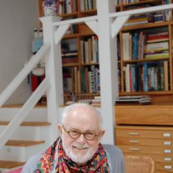 photo of children's book author and illustrator Tomie de Paola at a wooden table with shelves of books in the background