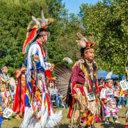 A group of four men in traditional regalia walking in a line outdoors.