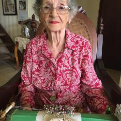 A woman with grey hair and glasses wearing a red and white paisley shirt. In front of her is lace and colorful pins